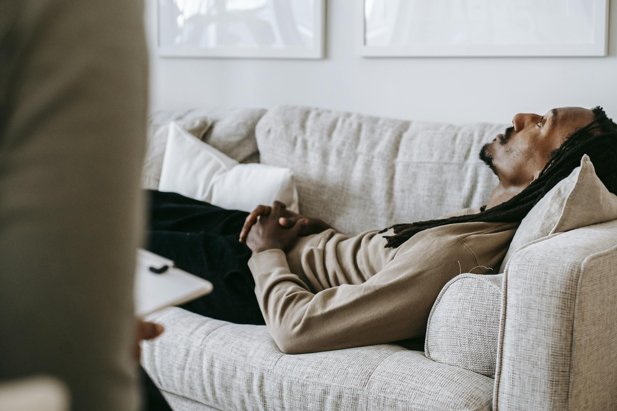 Man in therapy session lying on sofa, conversing with therapist in a relaxed indoor setting.